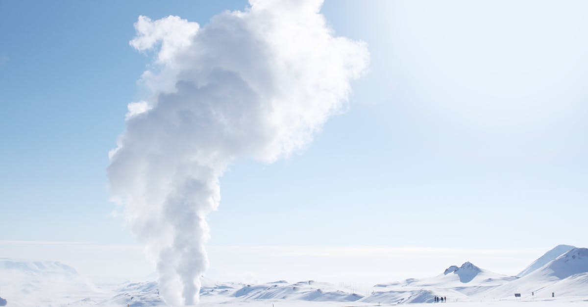 Snow-covered Icelandic landscape featuring geothermal steam plume against clear sky.